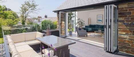 A modern outdoor patio with a glass enclosure, a sofa, and a dining table.