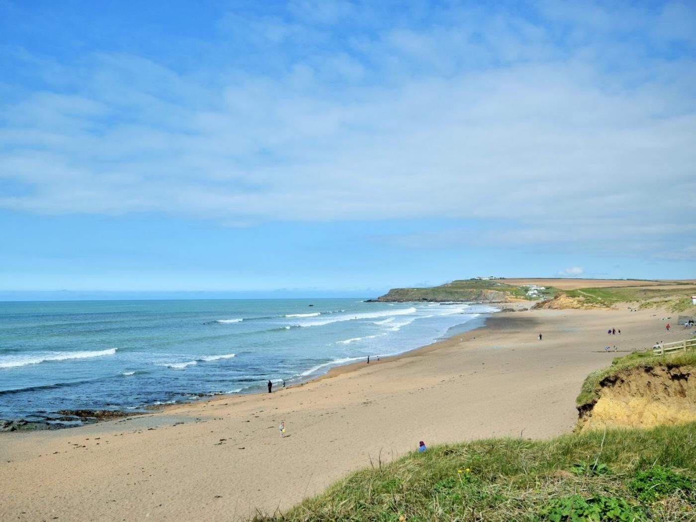 A coastal beach with a clear sky, a sandy shore, and a few people walking.
