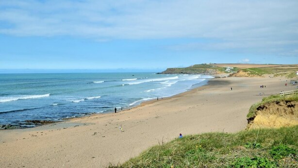 A coastal beach with a clear sky, a sandy shore, and a few people walking. - 2 Bed in Bude (oc-86152) (Widemouth Bay)