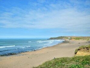 Ein Küstenstrand mit blauem Himmel, sandigem Ufer und einigen Spaziergängern.