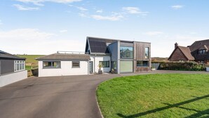 A modern two-story house with a paved driveway, a grassy lawn, and a neighboring traditional house. - 2 Bed in Bude (oc-86152) (Widemouth Bay)