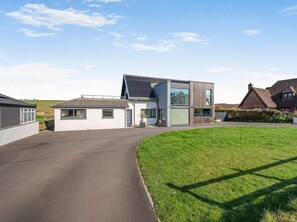 Ein modernes, zweistöckiges Haus mit gepflasterter Auffahrt, einem Rasen und einem angrenzenden traditionellen Haus.