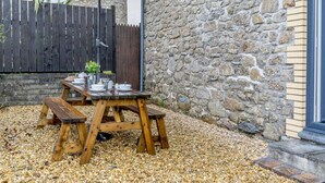 A wooden picnic table with an umbrella, set on gravel, against a stone wall and wooden fence. - 2 Bed in Clynderwen (oc-86158) (Clynderwen)
