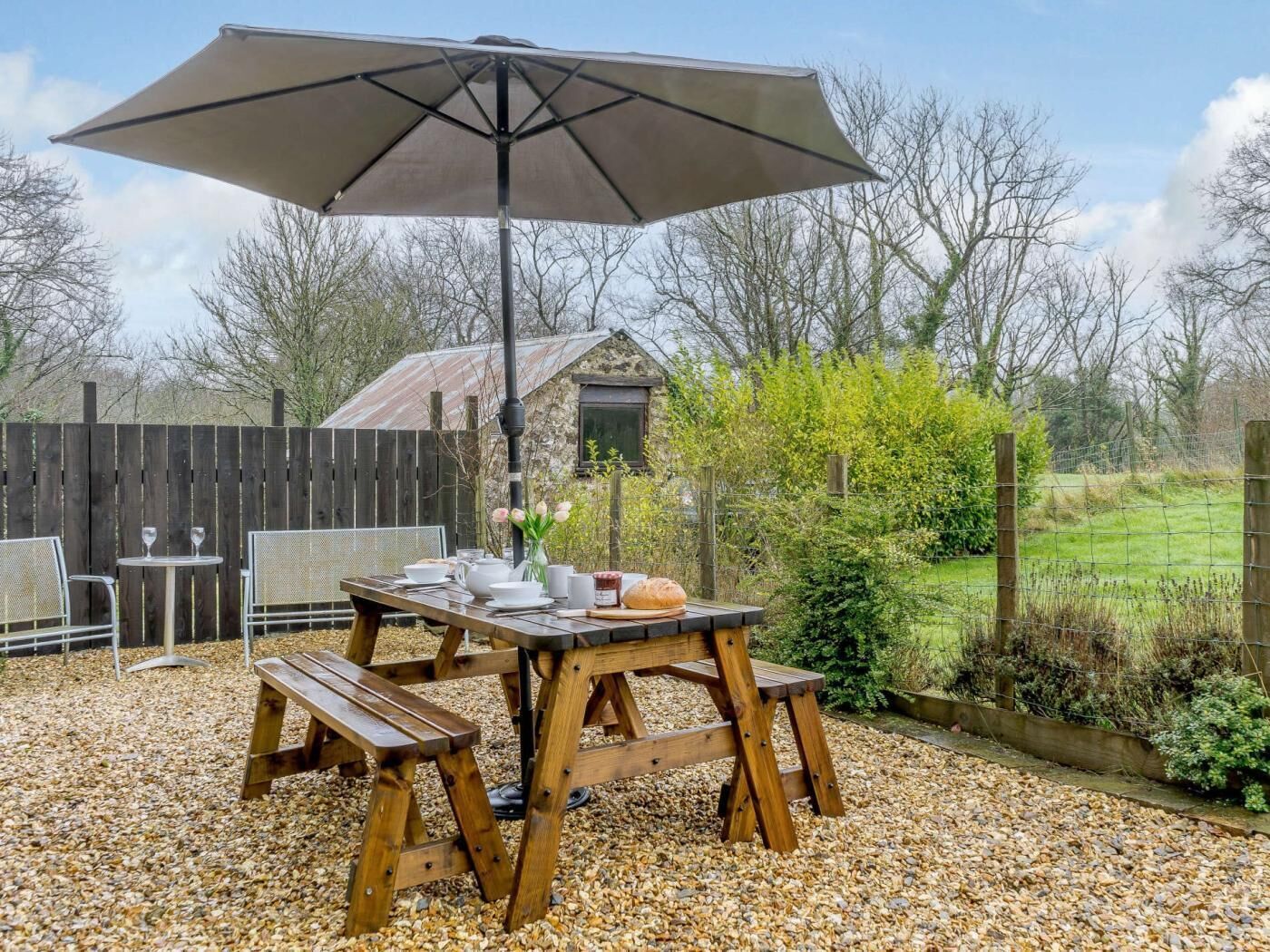 An outdoor patio with a wooden table, benches, and an umbrella.