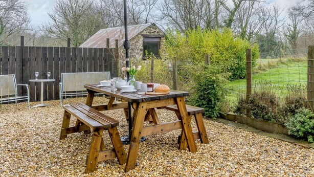 Eine Terrasse im Freien mit Holztisch, Bänken und Sonnenschirm.