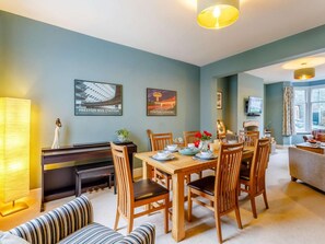 A dining area with a piano, wooden chairs, a table set for four, and a sofa. - 3 Bed in Keswick (oc-86162) (Keswick)