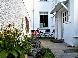 A white building with a window, a table with chairs, and a flamingo statue. - 3 Bed in Keswick (oc-86162) (Keswick)