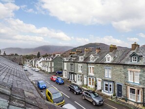 A row of stone houses with a street in front, parked cars, and a mountain in the background. - 3 Bed in Keswick (oc-86162) (Keswick)