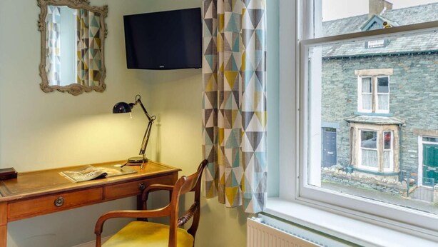 Een kamer met een bureau, stoel, televisie en een raam met uitzicht op een stenen gebouw.