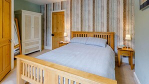 Een slaapkamer met een houten bed, twee nachtkastjes, een kledingkast en een deur.
