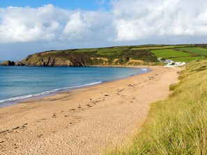Ein sandiger Strand mit Fußspuren, hügelige Wiesen und Blick aufs Meer.