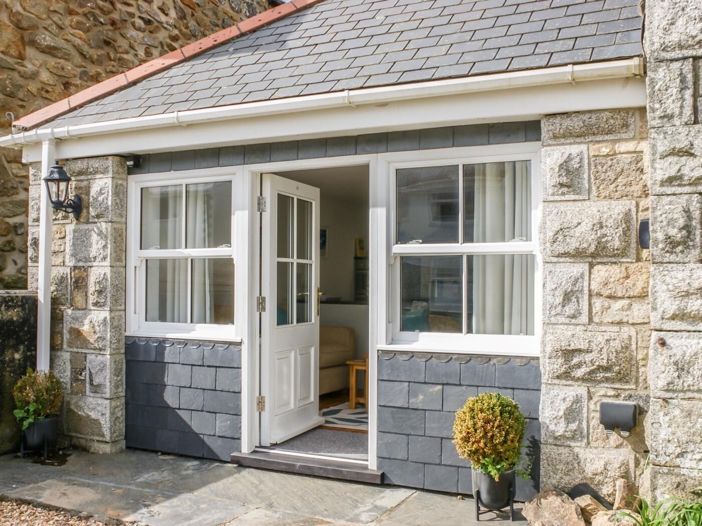 A stone building with a grey tiled roof, a white door, and two windows.