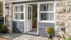 En byggnad av sten med ett grått tak täckt av takpannor, en vit dörr och två fönster.