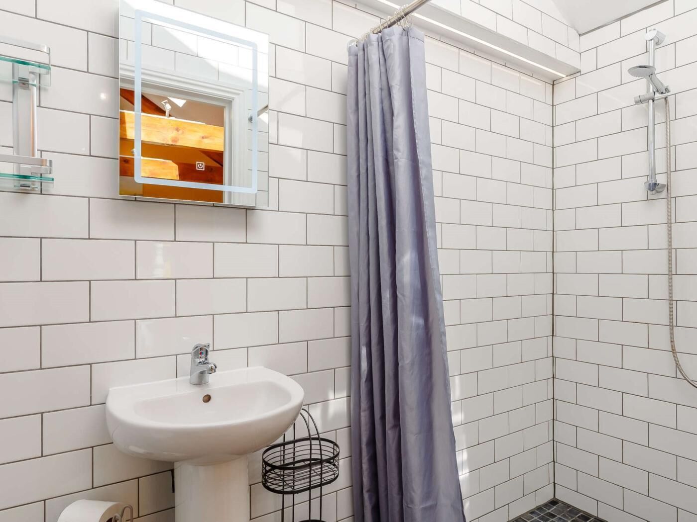 A bathroom with a white sink, a shower with a curtain, and a mirror with a wooden shelf.