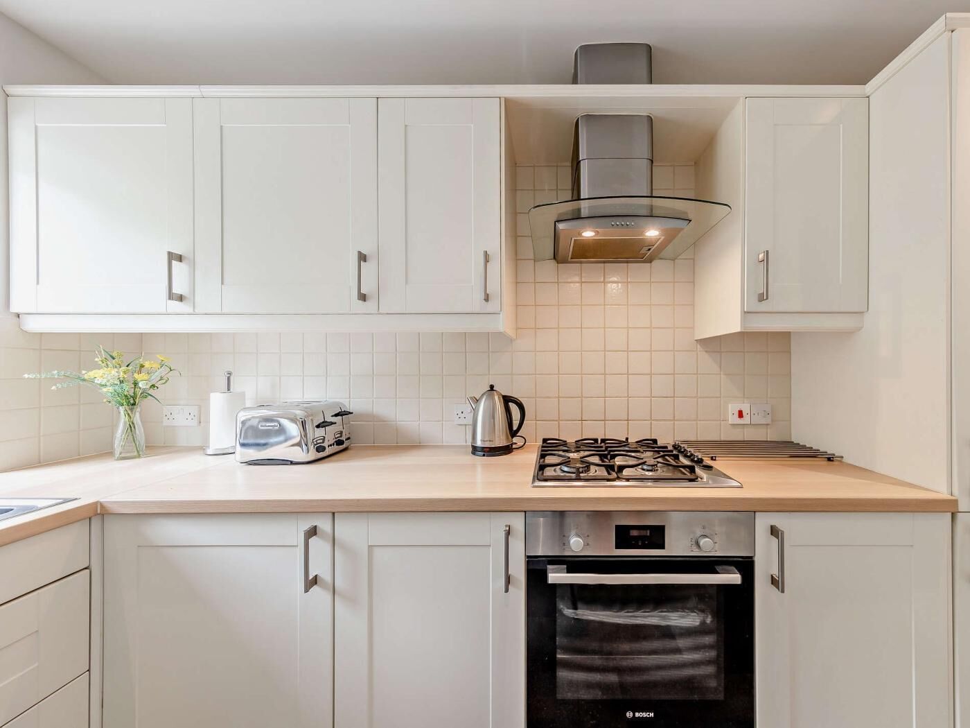 Una cocina moderna con gabinetes blancos, horno Bosch, estufa a gas, tostadora y hervidor.