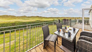 A balcony with wicker furniture, a table with cups, and a view of a green landscape. - 3 Bed in Aberdyfi (oc-dy007) (Aberdovey)