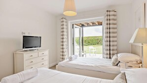 A bedroom with a bed, a TV on a dresser, a lamp, and a view of a garden. - 3 Bed in Aberdyfi (oc-dy007) (Aberdovey)