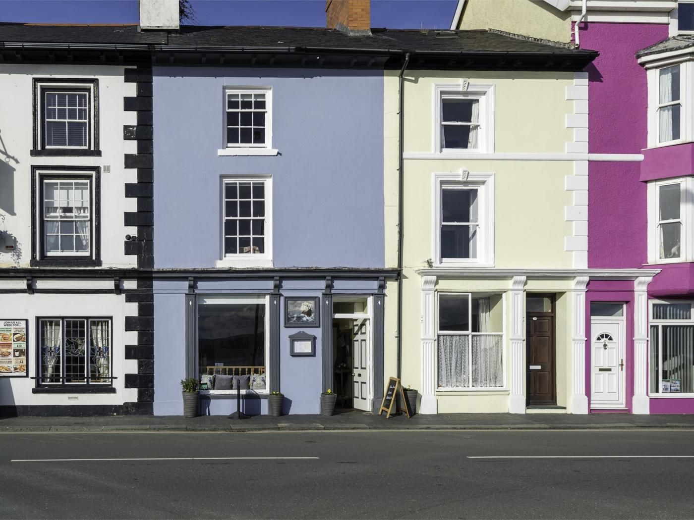 A row of colorful townhouses with distinct architectural styles, including a shop with a visible window display and signage.
