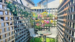 Ein kleiner Sitzbereich im Freien mit Holzlattenzaun, zwei Stühlen, einem Tisch und verschiedenen Blumentöpfen.