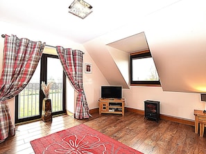 A room with a sloped ceiling, a television, a wooden cabinet, and a red rug. - 3 Bed in Perth (oc-86058) (Forgandenny)