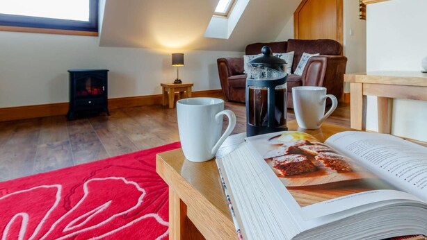 Ein gemütliches Zimmer mit Dachfenster, einer Kaffeemaschine, einem roten Teppich und einer Zeitschrift auf einem Tisch.