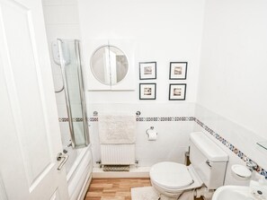 Een badkamer met douche, toilet en wastafel, met witte tegels en een decoratieve rand.