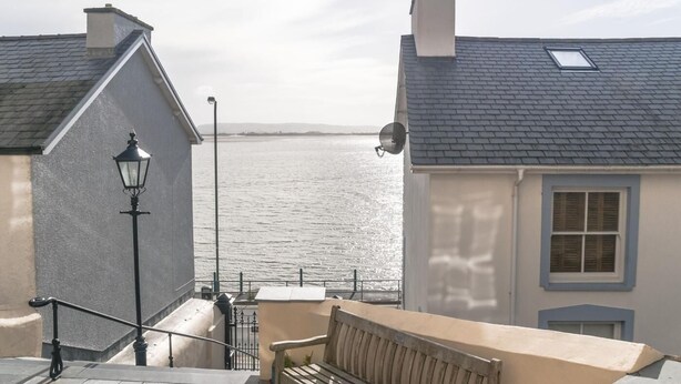 En byggnad vid kusten med en bänk, en lyktstolpe och utsikt över havet.