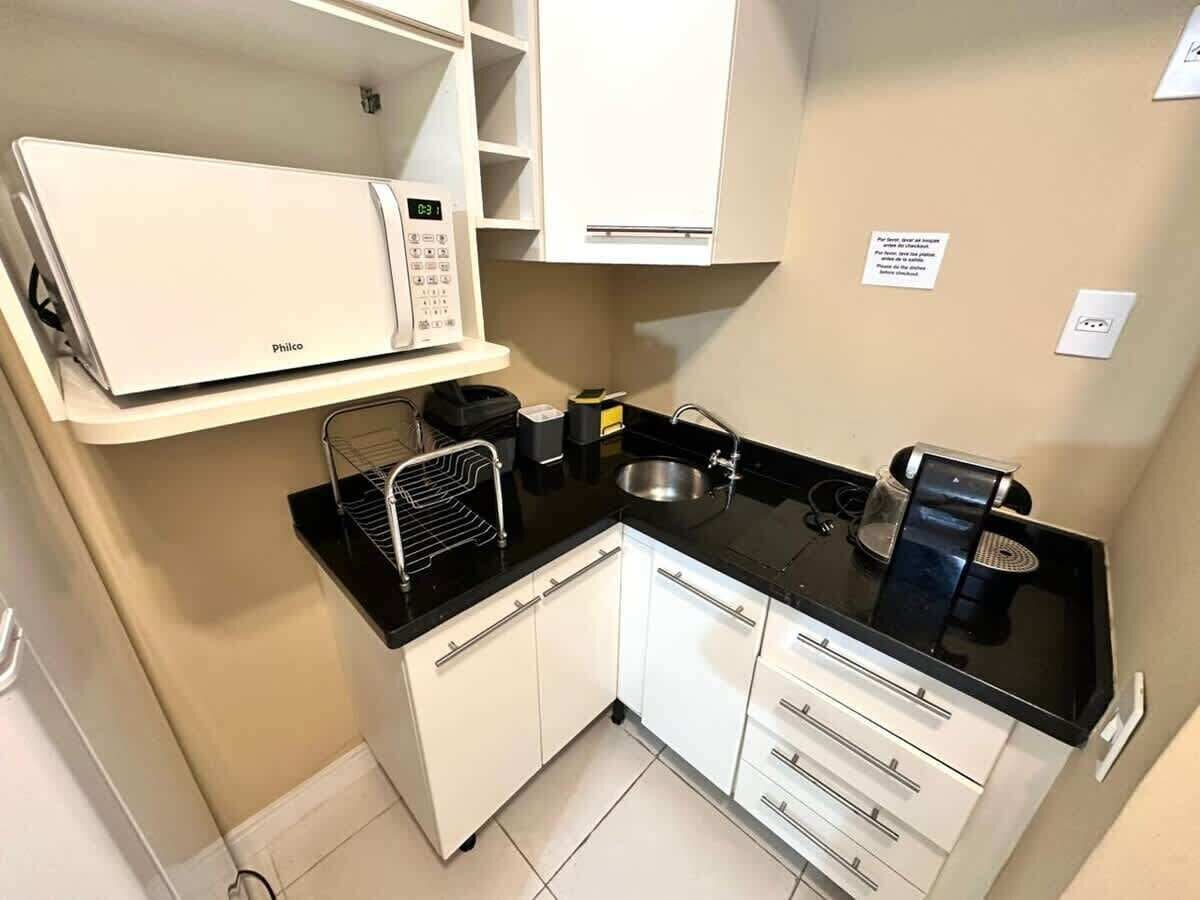 A compact kitchen with white cabinets, a black countertop, a microwave, a coffee maker, and a sink.