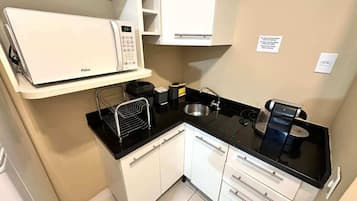 A compact kitchen with white cabinets, a black countertop, a microwave, a coffee maker, and a sink.