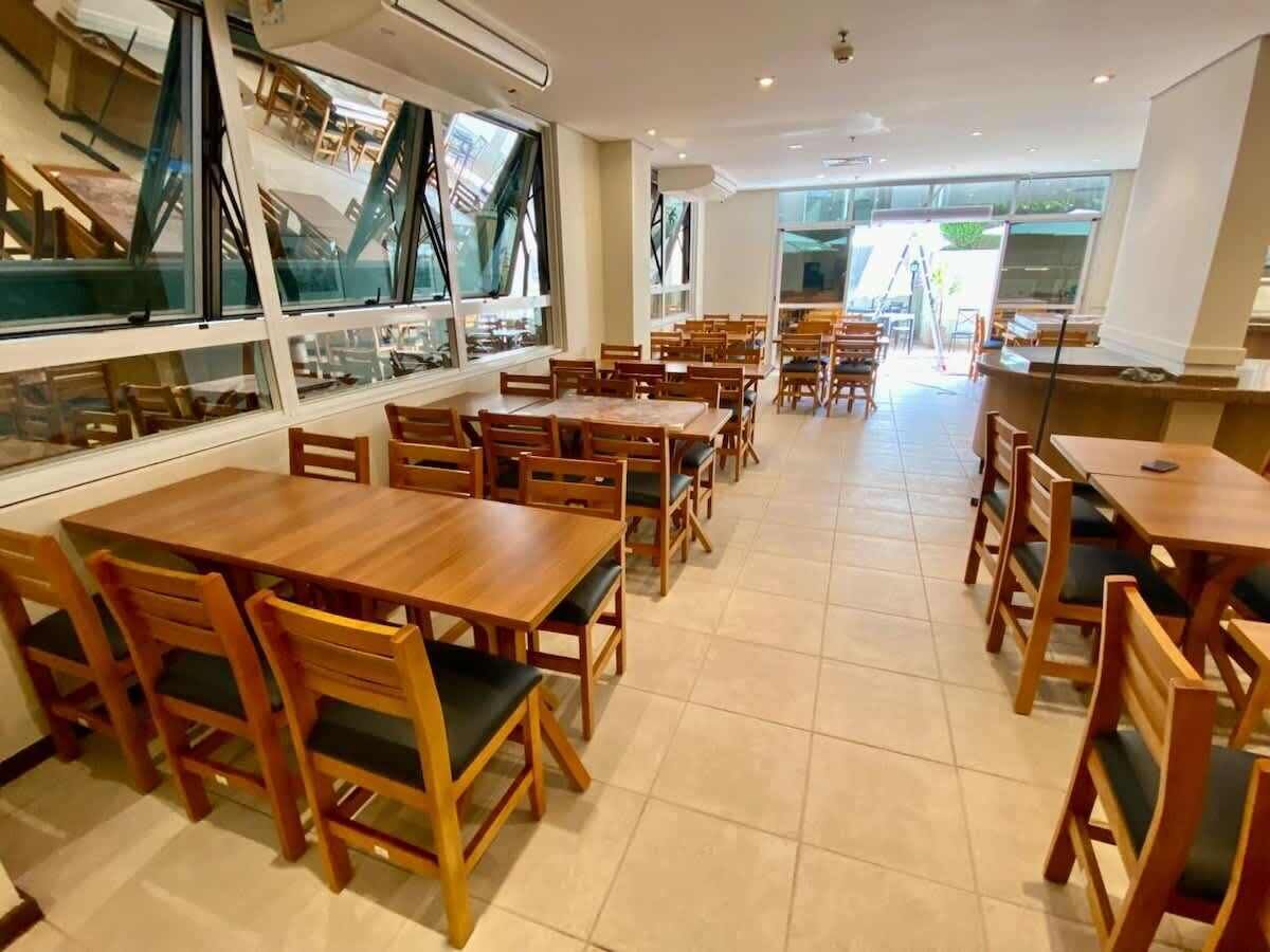 Ein Restaurant mit mehreren Holztischen und -stühlen, großen Fenstern und einem gefliesten Boden.