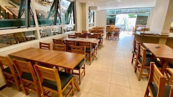 Ein Restaurant mit mehreren Holztischen und -stühlen, großen Fenstern und einem gefliesten Boden.