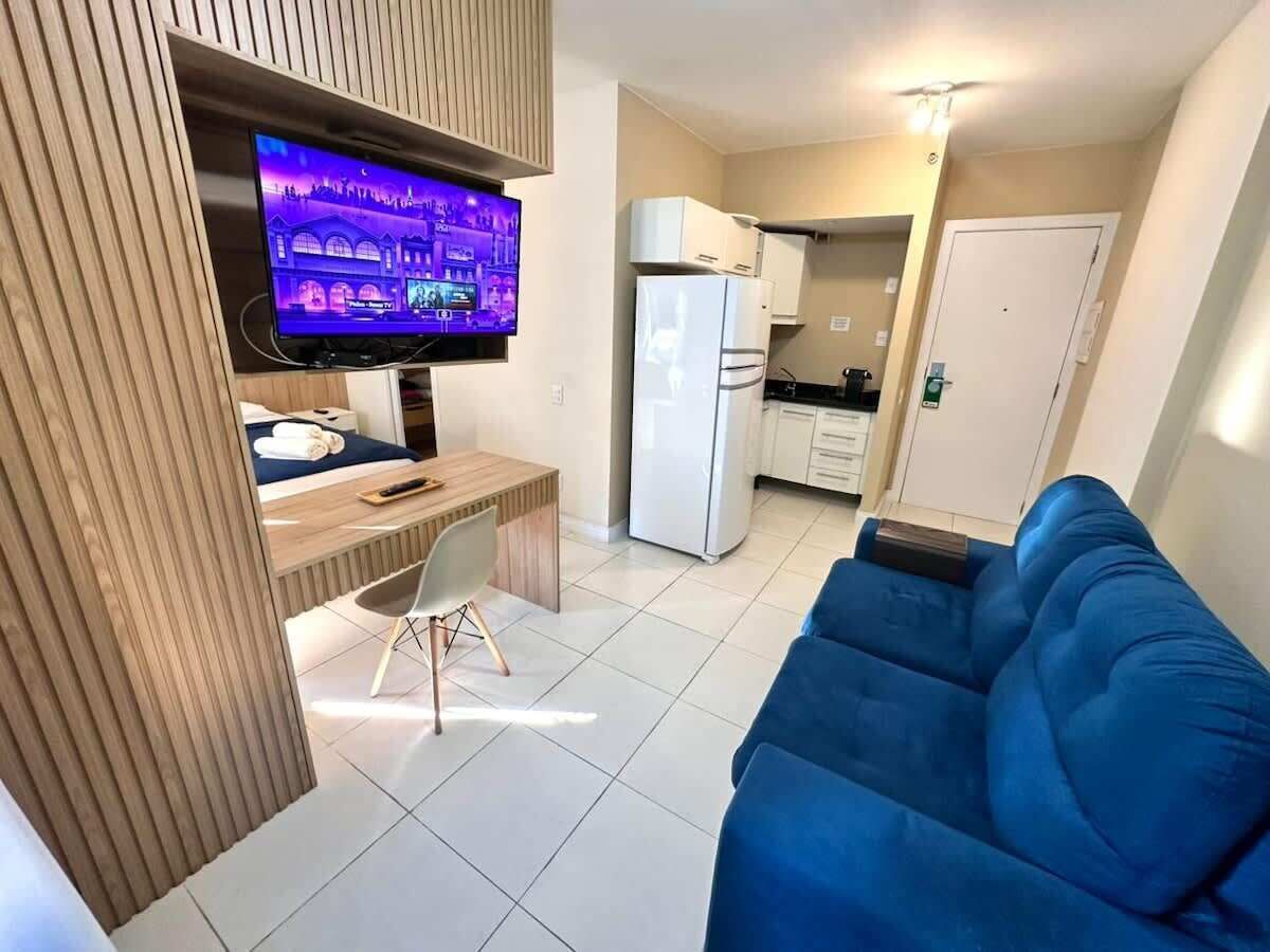 Un espacio habitable compacto con televisor, zona de comedor, kitchenette y sofá azul.