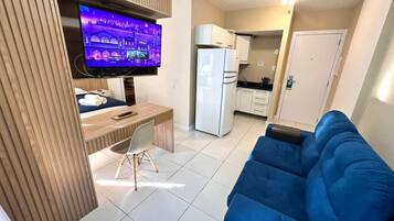 Un espacio habitable compacto con televisor, zona de comedor, kitchenette y sofá azul.