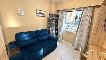 A living room with a blue sofa, a clock on the wall, and a window with curtains.