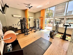Un gimnasio con equipo de ejercicio, una colchoneta negra y ventanas amplias.