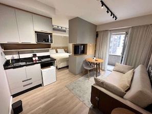 Habitación de hotel compacta con kitchenette, cama, zona de estar y televisor.