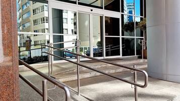 A modern building entrance with a glass facade, metal handrails, and a concrete ground.