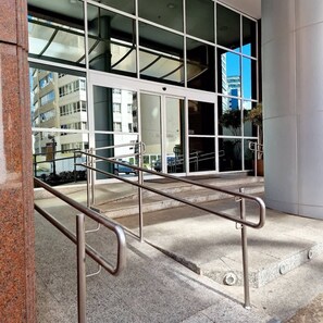 A modern building entrance with a glass facade, metal handrails, and a concrete ground.