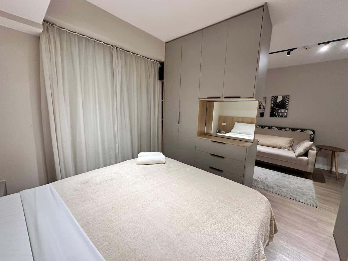 A modern bedroom with a bed, a bedside table, a wardrobe, and a mirror.