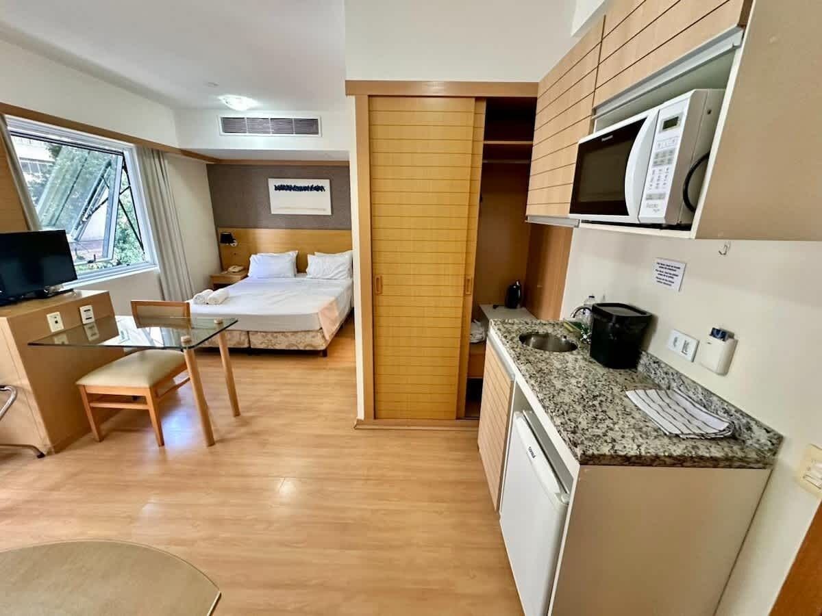 Habitación de hotel pequeña con kitchenette, una cama, un rincón de comedor y una ventana.