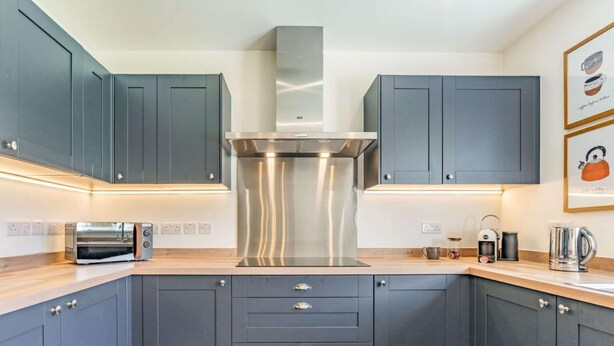 A modern kitchen with grey cabinets, a stainless steel range hood, a toaster, and a kettle on the countertop. - 3 Bed in Penrith (oc-86724) (Hackthorpe)