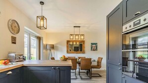 A modern kitchen with dark cabinetry, a built-in oven, and a dining area with a table and chairs. - 3 Bed in Penrith (oc-86724) (Hackthorpe)