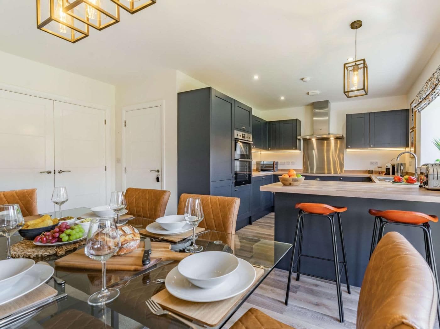 A modern kitchen with dark cabinetry, a central island, and a dining area with a glass table and leather chairs.