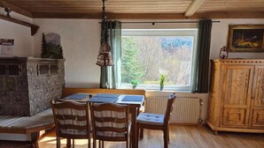 Ett matbord i trä med stolar, en bänk, ett skåp och ett fönster med utsikt över träd.