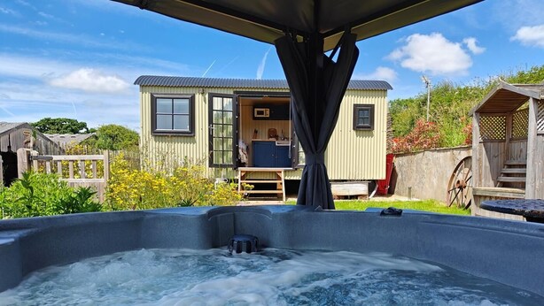 Un bain à remous avec une terrasse en bois, un petit bâtiment doté d’une fenêtre et d’une porte, et une clôture en bois en arrière-plan.