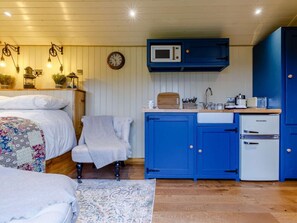Een gezellige kamer met een bed, een stoel, een kleine kitchenette met blauwe kastjes, een magnetron en een koelkast.