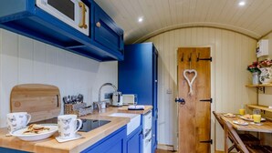 Une cuisine de taille réduite avec des meubles bleus, une porte en bois ornée d’un motif en forme de cœur, et une table de petit-déjeuner avec de la nourriture et des boissons.