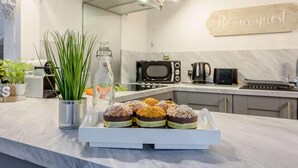 Et moderne køkken med bordplade i marmor, kaffemaskine, mikrobølgeovn og et skilt med teksten 'Vær vores gæst'.