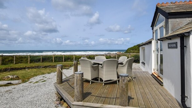 Eine Holzterrasse mit Sitzgelegenheit, Blick aufs Meer und ein Gebäude mit der Aufschrift 'THE NOOK'.