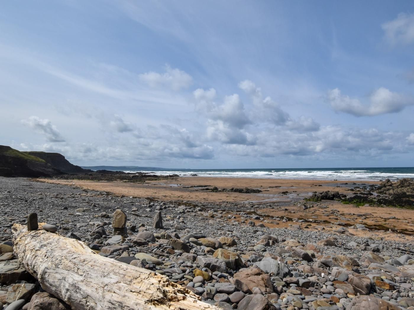 A rocky beach with a large log in the foreground and a view of the ocean under a cloudy sky.